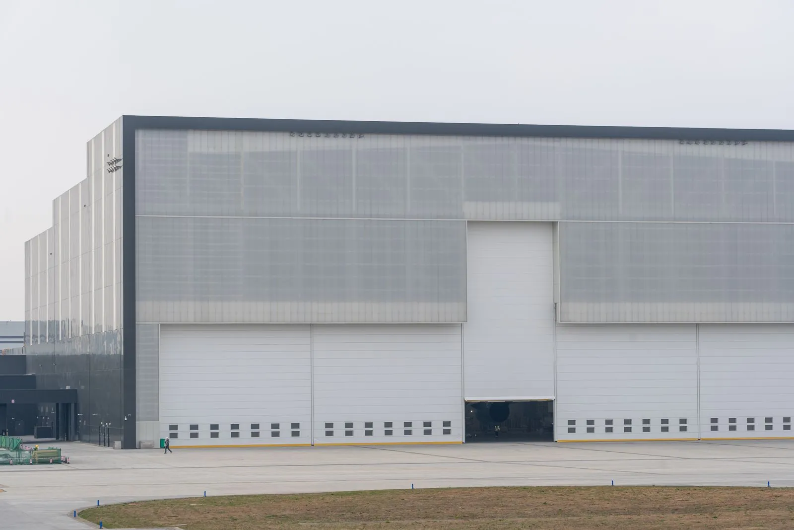 A white warehouse with a single large door under a flat grey sky